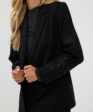 Load image into Gallery viewer, Make a stylish and confident statement with our EsQualo blazer. This timeless black blazer features exquisite beaded detailing on both sleeves, adding a touch of elegance to any outfit. This must-have piece belongs in every fashion-savvy closet and will remain a staple for years to come. Pictured paired with our Senia Skirt Embellishment in Black - EsQualo W2405720. A perfect match!
