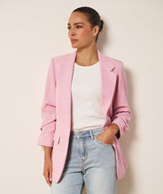 Load image into Gallery viewer, Woman wearing a pink blazer, white shirt, and light blue jeans against a beige background.

