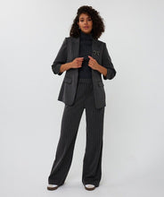 Load image into Gallery viewer, Woman wearing a dark gray pinstripe suit, black turtleneck and white and black sneakers against a white background.
