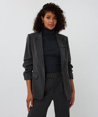 Woman wearing a dark gray pinstripe suit against a white background.