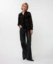 Load image into Gallery viewer, Woman wearing a sheer black  blouse with black velour floral pattern and gold lurex threading,   black pants, black star earrings and black shoes against a white background.
