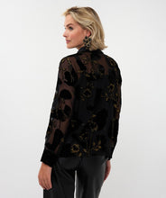 Load image into Gallery viewer, Woman wearing a sheer black  blouse with black velour floral pattern and gold lurex threading,  black pants and black star earrings against a white background.
