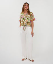 Load image into Gallery viewer, Woman wearing a colorful jungle patterned short sleeve blouse and white pant against a white background.
