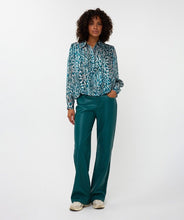 Load image into Gallery viewer, Woman wearing a teal and white with shimmer patterned blouse, teal pants and white sneakers against a white background.

