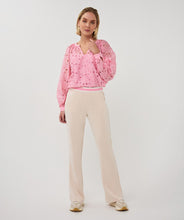 Load image into Gallery viewer, Woman wearing a pink eyelit blouse and tan pants against a grey background.
