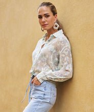 Load image into Gallery viewer, Woman wearing a sheer floral blouse, silver drop earrings and light blue jeans against a beige wall.
