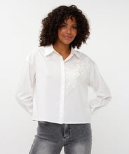 Load image into Gallery viewer, Woman wearing a white blouse with floral embroidery and jeans against a white background.
