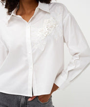 Load image into Gallery viewer, Model wearing a white blouse with floral embroidery and jeans against a white background.
