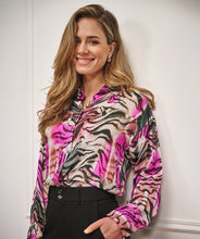 Load image into Gallery viewer, Woman wearing a colorful zebra patterned blouse and black pants against a white wall.
