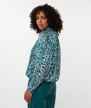 Load image into Gallery viewer, Woman wearing a teal and white with shimmer patterned blouse and teal pants against a white background.
