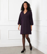 Load image into Gallery viewer, Woman wearing a dark purple and metallic dress and black heels standing against a white paneled wall.
