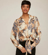Load image into Gallery viewer, Woman wearing a tie waist patterned long sleeve blouse in floral grey, cream and tan and black pants against a neutral background.
