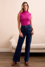 Load image into Gallery viewer, Woman wearing a pink sleeveless top, blue jeans and brown boots standing against a beige wall with a beige chair in the background.
