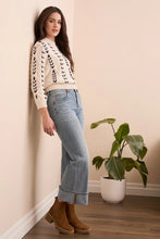 Load image into Gallery viewer, Woman wearing a patterned sweater, palazzo jeans, and brown boots standing in a room with a plant.
