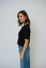 Load image into Gallery viewer, Woman wearing a black knit top with a white collar and blue jeans against a plain background.
