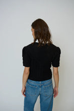 Load image into Gallery viewer, Woman wearing a black knit top with a white collar and blue jeans against a plain background.
