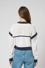 Load image into Gallery viewer, Woman wearing an ivory sweater cardigan with navy accents and blue jeans against a grey background.
