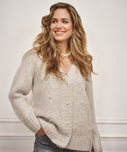 Load image into Gallery viewer, Woman wearing a light sand sweater  with pearls and feathers, grey pants and pearl necklace against a white wall.
