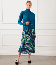 Load image into Gallery viewer, Woman wearing a teal blue cardigan over matching teal turtleneck top, colorful skirt and black heels against a white wall.
