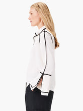 Load image into Gallery viewer, This stunning and unique blouse is a bold choice for fashion lovers who like to stand out. The black trim along the seams creates a striking contrast with the off-white fabric. The pearl buttons add a touch of elegance, while the flounce sleeves have slits at the end for extra flair. The blouse has a classic shirt collar and a hip-length hem.
