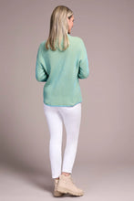 Load image into Gallery viewer, Woman sitting on a wooden stool wearing a teal blue sweater, white leggings against a pale pink background.
