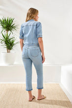 Load image into Gallery viewer, Woman wearing a short sleeve, light blue denim jacket, jeans and gold sandals standing in a minimalistic room with a plant.
