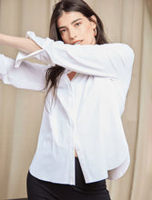 Load image into Gallery viewer, A woman wearing a white long-sleeve button-up shirt and black pants, posing with her arms crossed in front of a beige curtain background.
