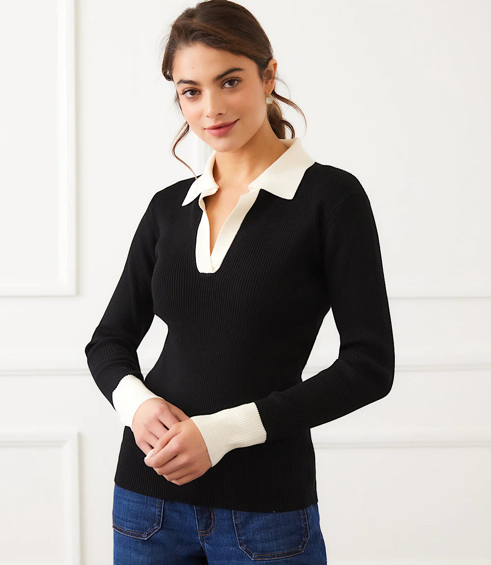 Woman wearing a black sweater with white collar and cuffs and jeans against a white background.
