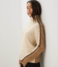 Load image into Gallery viewer, Woman wearing a color block turtleneck sweater with black contrast stitching down the arms and black pants standing against a white wall.
