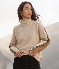 Load image into Gallery viewer, A woman wearing a color block sweater with black contrast stitching down the sleeves and dark jeans photographed outdoors against a soft-focus mountain background.
