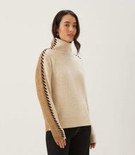 Load image into Gallery viewer, Woman wearing a color block turtleneck sweater with black contrast stitching down the arms and black pants standing against a white wall.
