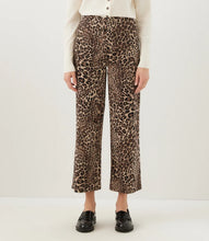 Load image into Gallery viewer, A model is shown from the waist down wearing high-waisted, wide-leg cropped trousers with a brown and beige cheetah print pattern, styled with a cream long-sleeve top and black loafers.
