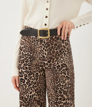 Load image into Gallery viewer, A person wearing cheetah print trousers with a black belt featuring a gold buckle, styled with a cream button-up top against a plain white background.
