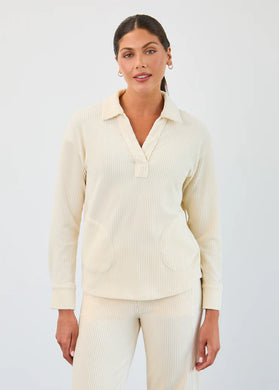 Woman wearing small gold hoop earrings, creme corduroy long sleeve, V-neck top and matching pant against a neutral background.