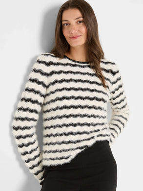 Woman wearing a black and cream striped fuzzy sweater and black pants against a plain background.