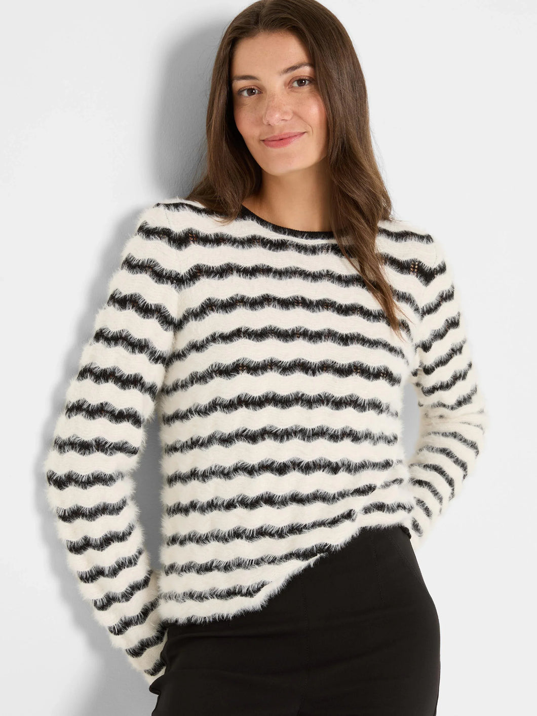 Woman wearing a black and cream striped fuzzy sweater and black pants against a plain background.