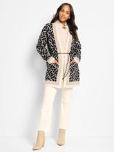Load image into Gallery viewer, Woman wearing a patterned long jacket over a beige sweater, white pants and suede beige boots against a white background.
