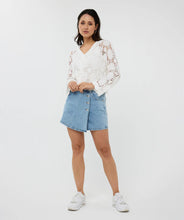 Load image into Gallery viewer, Woman wearing an off-white crochet cardigan over a white tank, blue jean mini skirt and white sneakers against a white background.

