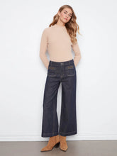 Load image into Gallery viewer, Woman wearing a beige sweater, dark blue jeans and suede boots against a white background.
