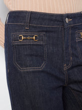 Load image into Gallery viewer, Close-up of dark indigo denim jeans with a gold horsebit detail on the back pocket, worn with a beige ribbed top.
