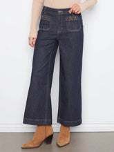 Load image into Gallery viewer, A person wearing dark blue wide-leg cropped jeans with a beige ribbed sweater and tan ankle boots, standing against a white wall.
