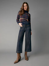 Load image into Gallery viewer, A model stands against a gray studio background wearing a dark blue wide-leg cropped denim pair with front patch pockets, a navy and burgundy plaid turtleneck sweater, and brown pointed-toe ankle boots.
