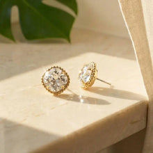 Load image into Gallery viewer, Gold earrings with clear gemstones on a light stone surface with a leaf in the background.
