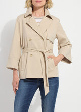 Load image into Gallery viewer, Woman wearing a beige trench and blue jeans against a white background.
