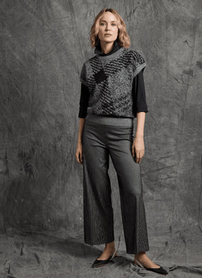 Woman wearing a patterned sweater, black sheen line jeans against a textured gray background.