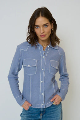 Woman wearing a light blue western style sweater top and blue jeans against a gray background.