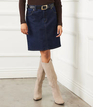Load image into Gallery viewer, Model wearing a dark blue denim skirt, brown top, black belt and beige knee-high boots against a white wall.
