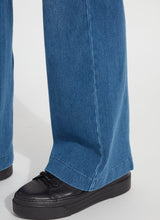 Load image into Gallery viewer, Close up of seam and hem of mid wash blue denim trouser and black shoes against a white background.
