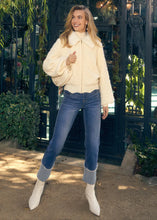 Load image into Gallery viewer, Woman carrying an off-white purse and wearing a creme jacket, blue jeans with pearl embellishments and off-white boots standing in front of a building.
