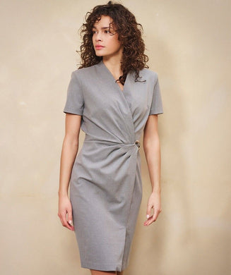 Woman wearing a gray cinched dress with silver buckle against a beige background.